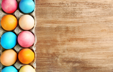 Cardboard container with colorful Easter eggs on wooden table