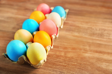 Cardboard container with colorful Easter eggs on wooden table