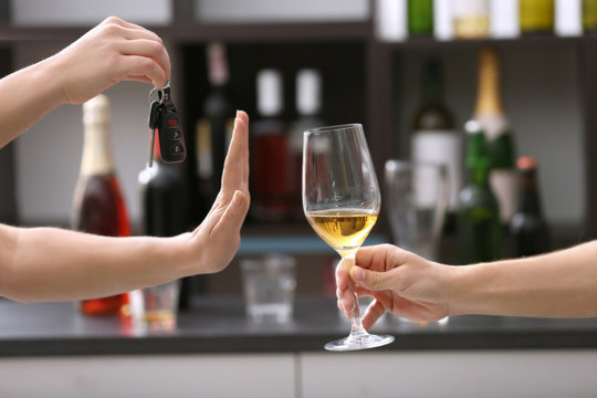 Woman with car key refusing glass of alcoholic beverage, on blurred background. Don't drink and drive concept