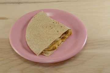 Peanut butter sandwich with whole wheat tortilla bread on pink plate