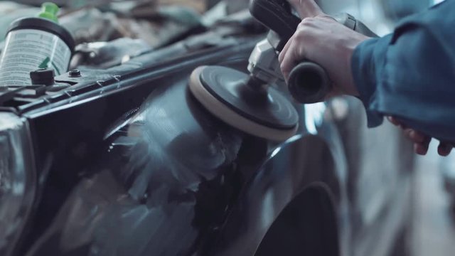 Mechanic using a rotary polisher on a the paintwork of a black car in a body shop to finish off a repair after an accident