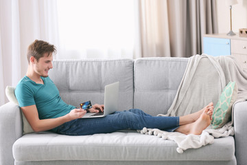 Obraz premium Young man online shopping with credit card on laptop, relaxing on sofa at home, e-commerce and digital payment