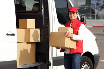 Young male courier with parcels near delivery service van