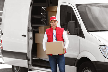 Young male courier with parcel near delivery service van