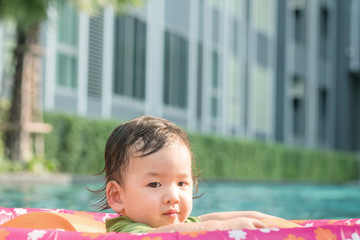 Closeup a baby boy sit in a boat for children in the swimming pool and building view background