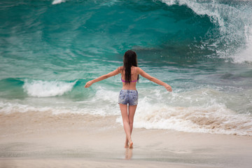 Fototapeta premium Attractive slime girl standing on sand beach with arms wide open on the big turquoise ocean wave background.