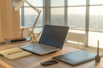 Side view picture of studio workplace with blank notebook, laptop. Comfortable work table, home office.