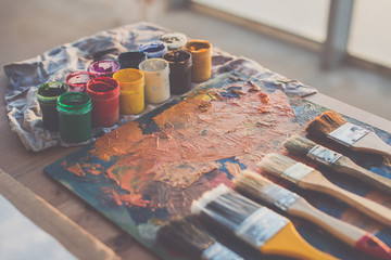 Painter workplace. Palette with brushstrokes and paintbrushes. Colorful gouache, crayons sets