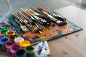 Obraz premium Side view of pallet with oil paint brushstrokes under paintbrush set in an art studio.