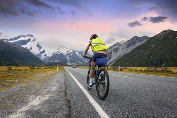 cyclist rides along the asphalt mountain road of Mount Cook New zealand, on a background of beautiful sky with cloud and snowy Southern Alps