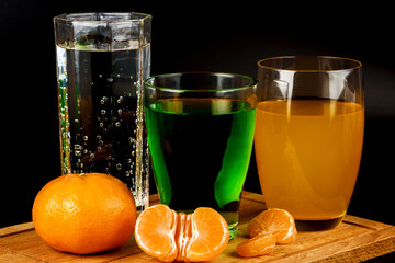 Fruit salad, segments of tangerine and glass with drink on a black background.