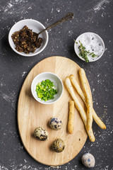 Quail eggs with salt, sauce, bread sticks, and green onions on a snack   dark background. Top view