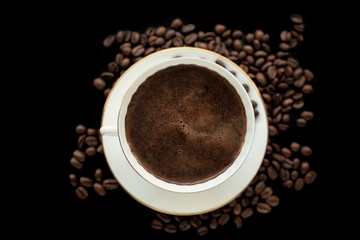 cup of black coffee with foam on background of roasted coffee beans