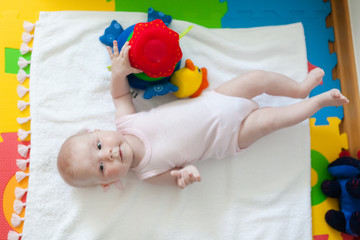 Cute baby girl lying on the floor playing with toys.
