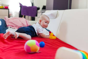 Cute baby girl playing with toys on the bed.