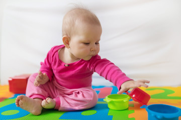 Cute bare feet  baby girl in pink clothes sitting on colorful puzzle play mat and playing with toys.