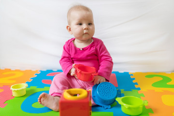 Cute bare feet  baby girl in pink clothes sitting on colorful puzzle play mat and playing with toys.