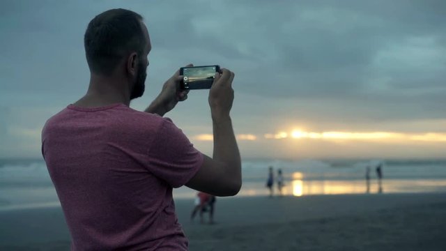 Young man taking photo of sunset and selfieon the beach, 4K
