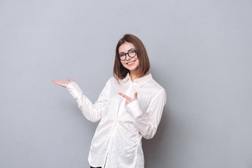 Smiling attractive young woman in eyeglasses pointing finger away