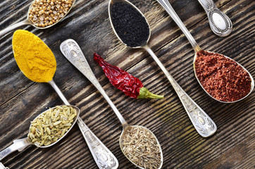 Assortment of spices in vintage spoons on wooden background..