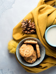 Mug of tea with milk and cookies with chocolate chips in a soft yellow winter scarf on gray background. Coffee break for home relax. Top view