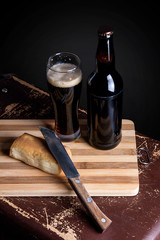 Glass and Bottle of dark beer with smoked cheese on cutting boar