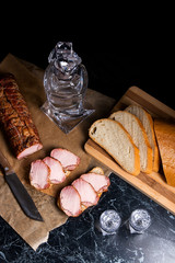 Bottle and shot glass with vodka with slices of smoked meat on b