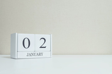 Closeup white wooden calendar with black 2 january word on blurred white wood desk and cream color wallpaper in room textured background with copy space , selective focus at the calendar