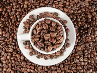 Background texture of coffee beans and a white espresso cup.