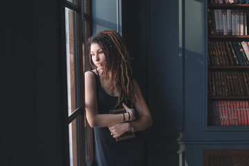 Obraz premium young girl in the library, standing the window in thought