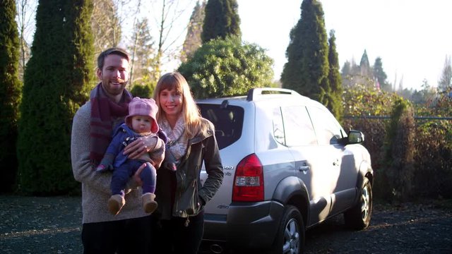 Portrait of a young mother, father and baby in front of their car with Christmas tree on top