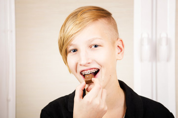 Teen with braces on his teeth eats chocolate. Orthodontics and bite correction.