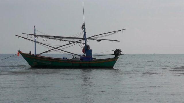 A Thai Squid Boat. The current rushes past and causes a small squid boat to pull on it's anchor. It's sunrise and the shadows are low giving the scene a lazy atmosphere.