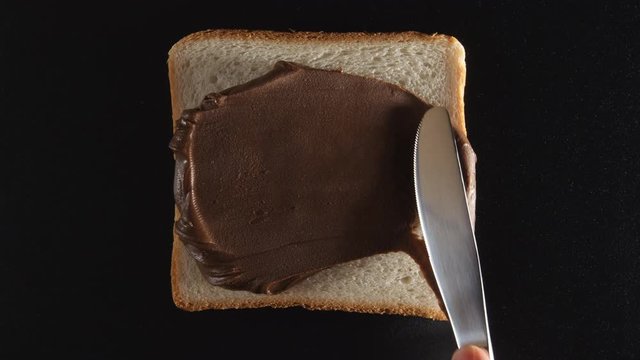 Human hand spreads a chocolate paste on a bread