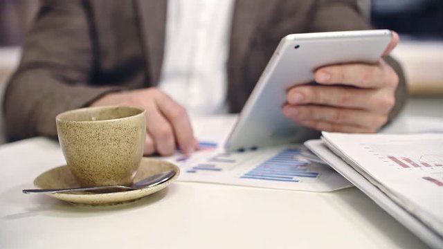 Closeup of businessman using digital tablet while waitress putting coffee cup and dessert on cafe table