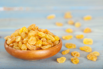 Golden raisins or dried grapes in wooden bowl, blue background