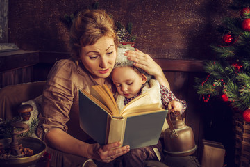 Mother reads to his son the book near a Christmas tree.