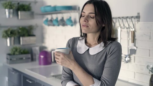 Young, pensive businesswoman drinking coffee in kitchen at home
