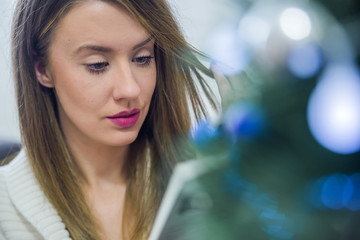 Thoughtful woman reading book in christmas decorated home. 