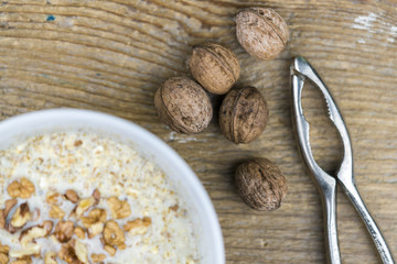 Whole fresh walnuts and a simple metal nutcracker alongside a bowl of cereal topped with chopped nuts