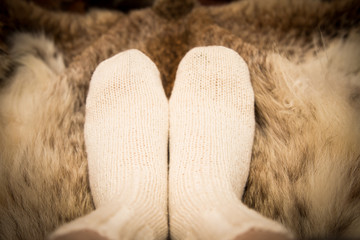 Warm hand knitted woolen socks on a fur background. First person view.