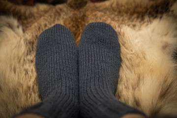 Warm hand knitted woolen socks on a fur background. First person view.