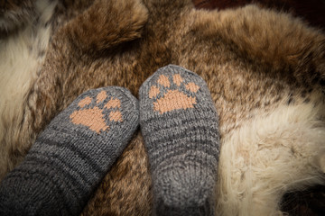 Fototapeta na wymiar Pair of a hand knitted woolen socks with a cat paw pattern on fur background