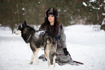 Beautiful young woman sitting and looking at husky dog in snow park