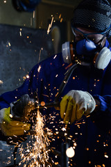 Industrial worker producing hot sparks while grinding steel metal pipe in workshop