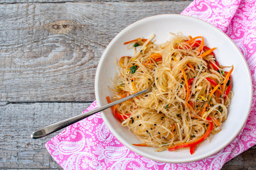 Rice noodles with vegetable stir fry on the ceramic bowl on dark wooden background