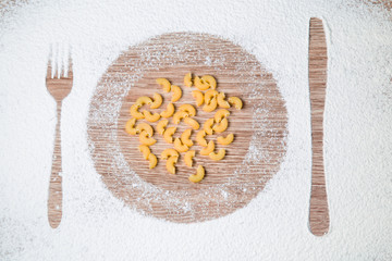 White flour on the wooden table. Prints of dish, fork and knife in the flour. Pasta in the center. Dietary food.