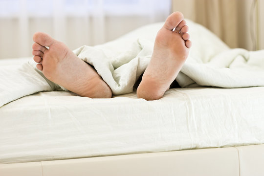 Men feet alone in a bed.