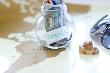 Travel budget - vacation money savings in a glass jar on world map. Preparation for travel, money, sunglass on the map.