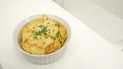 Potato fried snack have onion and salt in ceramic bowls, macro photo have background wood chair white color.